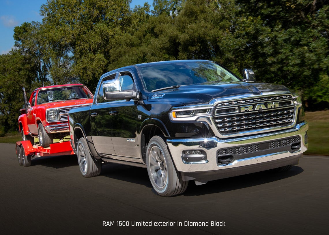 Front three-quarter view of a black Ram 1500 Limited towing a vintage truck on an open paved highway.