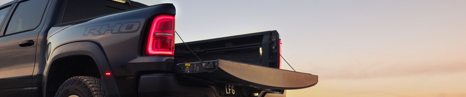 Rear three-quarter view of a black Ram 1500 RHO with open tailgate in a desert setting at sunset.
