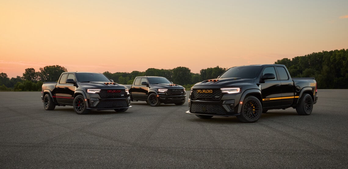 Front view of three black Ram 1500 TRX trucks parked on an asphalt lot at sunset.